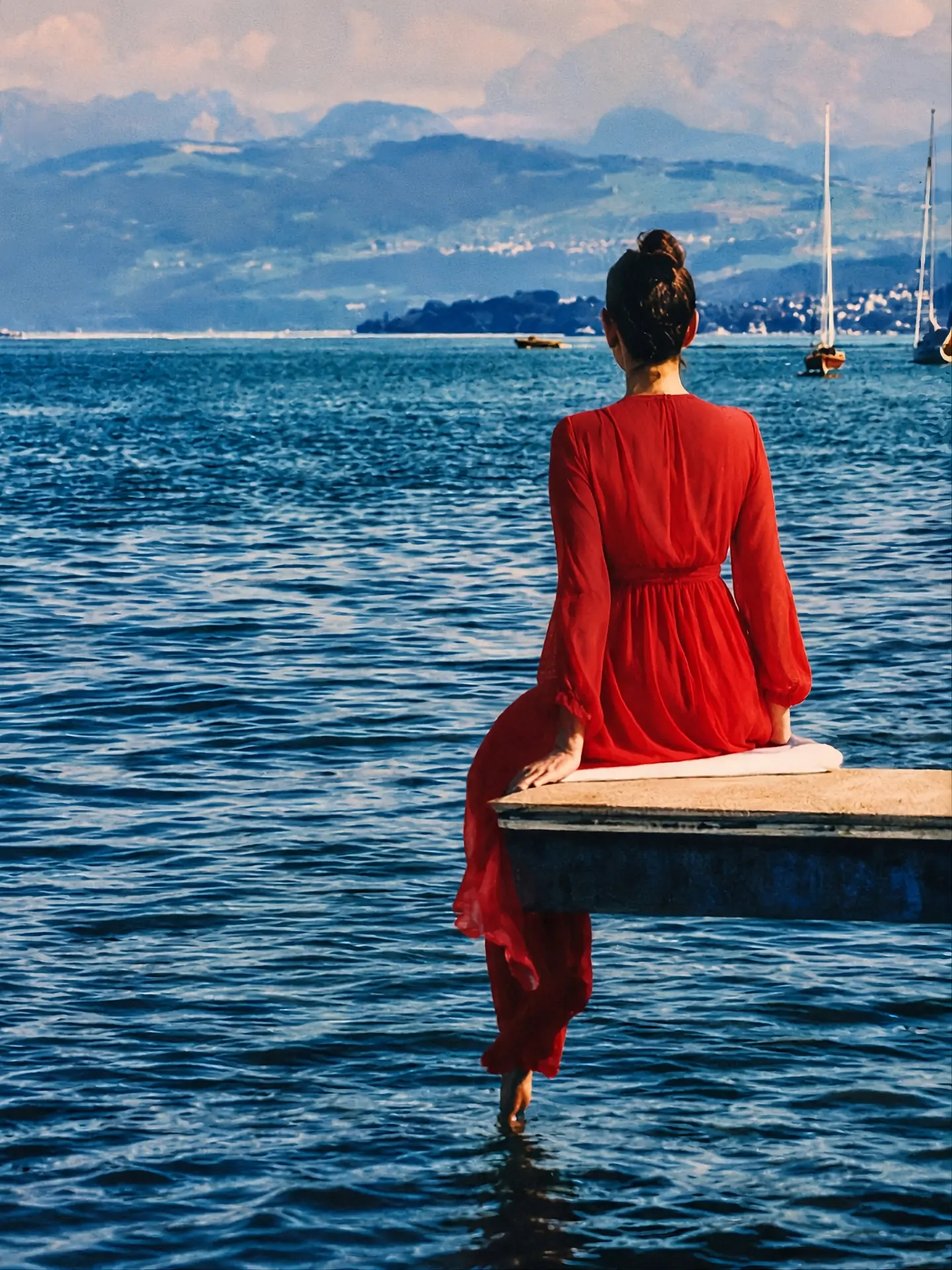 Anne Schaeflein in a red dress on a jetty, facing the lake