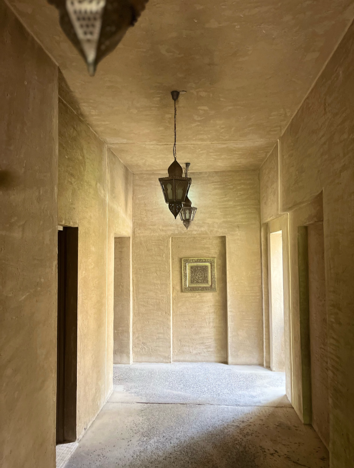 A lime-plaster corridor lit by hanging lanterns